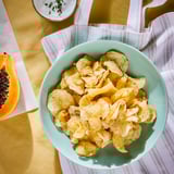 Blue bowl of potato crisps, white salt flecks, striped cloth background.