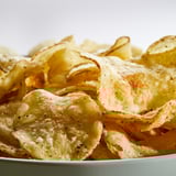A bowl of rustic potato crisps, lightly seasoned, with a golden color and slightly thick cut. Perfect for snacking.