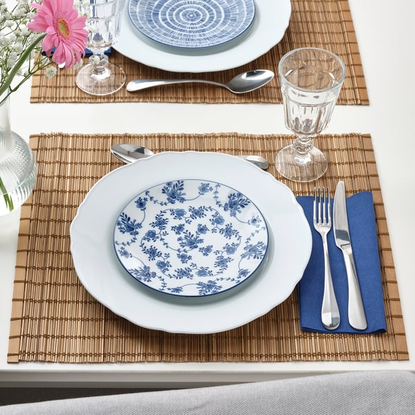 Table set with white plates featuring blue floral patterns, bamboo placemats, silverware, and glasses.