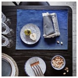 Blue table setting with plates, nuts, forks, glasses, and napkins on dark table.