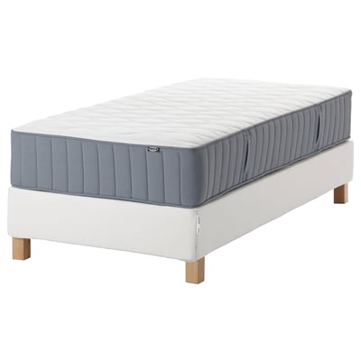A white bed set with a sleek, rectangular mattress and light wooden frame. The mattress has a quilted design with blue accents.
