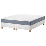 A white and blue mattress on a bed frame. The mattress has a padded surface and a visible spring system. The bed frame has light wooden legs.