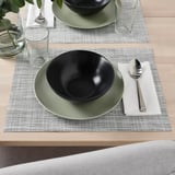 Two table settings with green plates, black bowls, glass cups, and silver spoons on placemats.