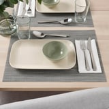 Table setting with two placemats, each holding a rectangular plate, a green bowl, silverware, and a glass.