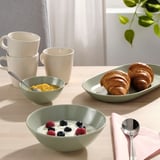 Table set with FÄRGKLAR bowls filled with yogurt and berries, croissants, and mugs for a breakfast meal.