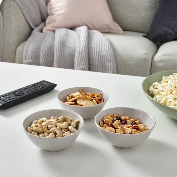 Four bowls of snacks and a tv remote on a white table, perfect for a relaxed movie night.