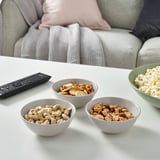 Four bowls of snacks and a tv remote on a white table, perfect for a relaxed movie night.