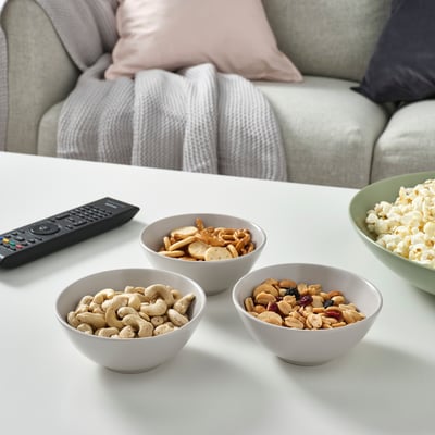 Four bowls of snacks and a tv remote on a white table, perfect for a relaxed movie night.