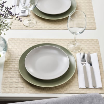 Two place settings with green and white plates, silverware, glass, napkins on woven placemats.