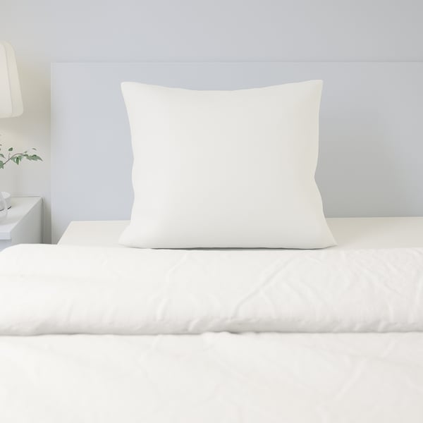 Bed with single white pillow and grey wall. Pillow is made of natural, breathable cotton.