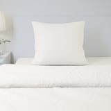 Bed with single white pillow and grey wall. Pillow is made of natural, breathable cotton.