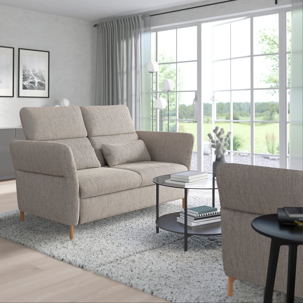 Modern living room with large window, grey FAMMARP sofa, adjustable headrests, wooden legs, cozy area rug, black coffee table, and books.