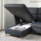 Sofa with lifted seat revealing storage, blanket inside. Adjustable headrest, wooden legs.