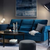 Modern living room with teal FAMMARP sofa, wooden coffee table, grey rug, and abstract wall art.