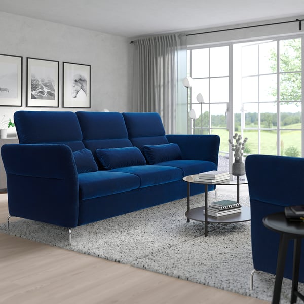 Modern living room with blue sofa, tables, large window, plants, and art.