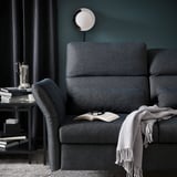 Dark grey FAMMARP sofa with adjust. Headrests, blanket, side table with books and coffee.
