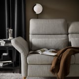 A modern gray FAMMARP sofa with adjustable armrests and cushions, a cozy brown throw blanket, and a side table with books and a decanter.