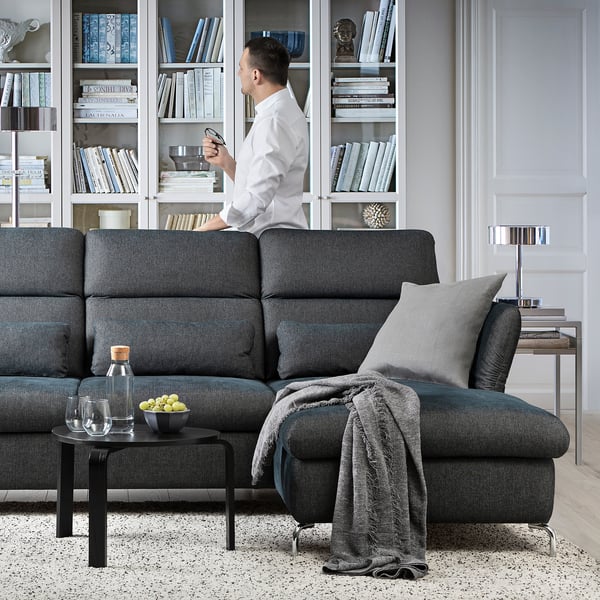 Modern living room with FAMMARP sofa and man with drink in front of bookshelf.