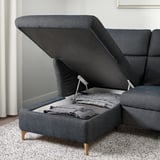 Gray sofas storage compartment open, showing folded blankets inside.