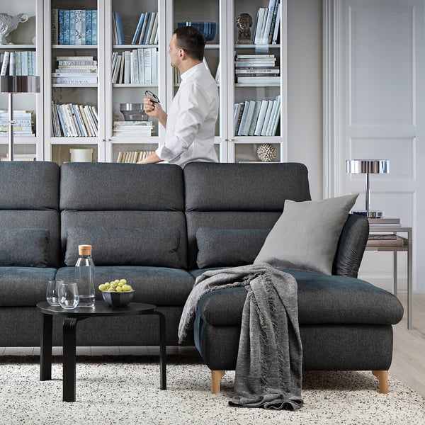 Modern living room: man on phone near FAMMARP sofa, wine glasses, books.