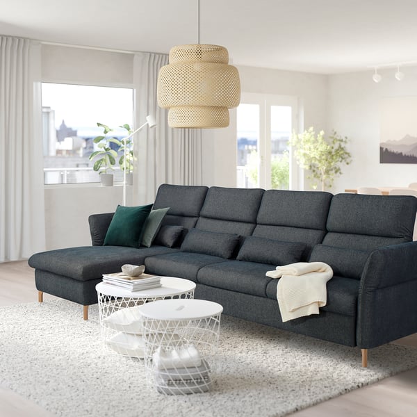 Modern living room: large grey FAMMARP sofa, green pillows, white side tables, woven pendant lamp, plants, city view.