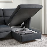 Sofa with open storage compartment, blankets inside, metal hinges, speckled rug visible.
