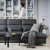 Modern living room with gray FAMMARP sofa, man standing, bookshelves, coffee table with wine glasses, and gray rug.