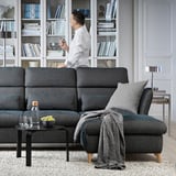 Modern living room with FAMMARP sofa, man on phone, bookshelf, coffee table, rug, pillows, blanket.