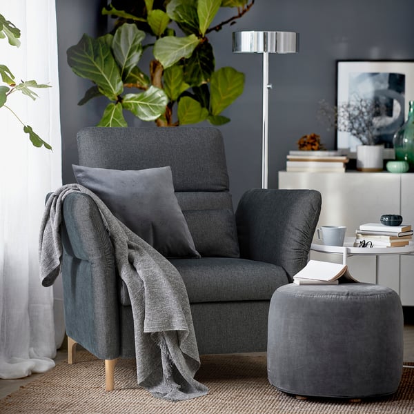 Cozy sitting area with dark gray FAMMARP armchair, gray throw, matching ottoman, plants, books, and floor lamp.