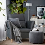 Cozy sitting area with dark gray FAMMARP armchair, gray throw, matching ottoman, plants, books, and floor lamp.