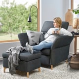 Woman relaxes in modern gray FAMMARP armchair, sipping coffee, with large window and green view.