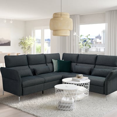 Modern living room with dark grey l-sofa, green cushions, side table, large window, rug, and bamboo lamp.