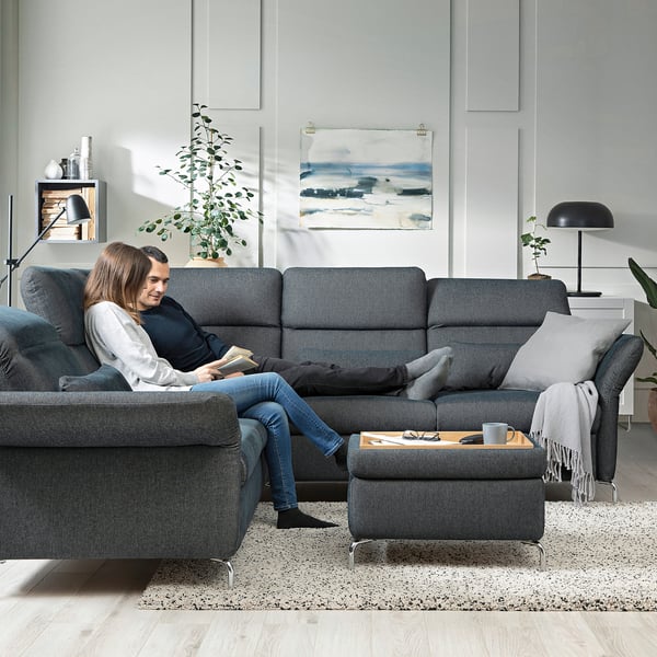 Cozy living room with a gray FAMMARP sofa, where a couple relaxes; soft lighting, abstract art, and plants enhance the modern minimalist decor.