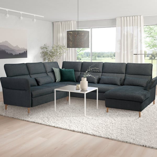 Modern living room with dark grey l-sofa, green pillows, plant.