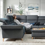 Woman relaxes on dark blue FAMMARP sectional sofa, grey throw, modern living room.