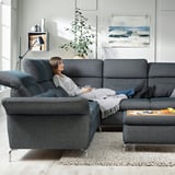 A modern, gray-blue FAMMARP sectional sofa with adjustable headrests and armrests in a cozy living room with a plant and abstract art on the walls.