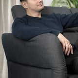 Man relaxes in black FAMMARP sofa with adjustable headrests.