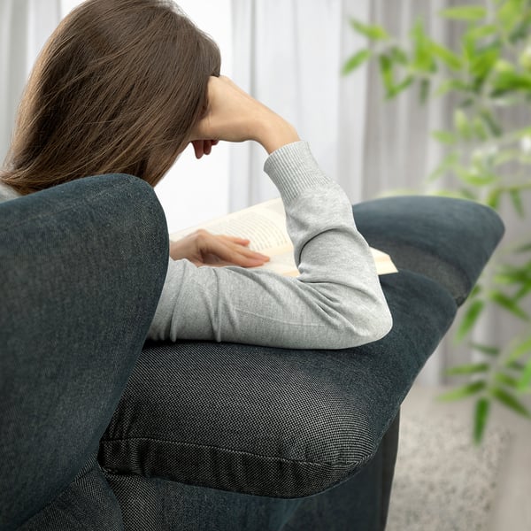 In a person sits on a green FAMMARP sofa, reading a book. The sofa adjustable headrests and lumbar support. A plant is visible to the right.