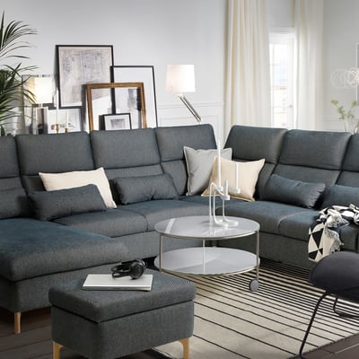 Modern living room with blue-gray FAMMARP sectional sofa, decorative pillows, round glass coffee table, and large window with white curtains.