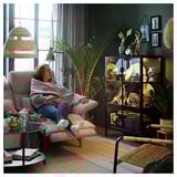 Woman relaxing on beige sofa in cozy green room with plants.