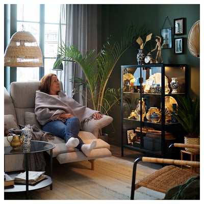 Woman relaxing on beige sofa in cozy green room with plants.