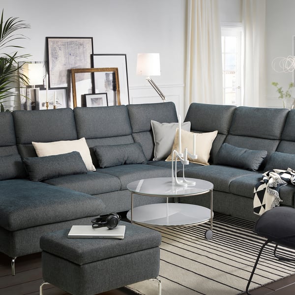 Modern living room with gray FAMMARP sectional sofa, glass coffee table, cushions, headphones, books, lamp, plants, and framed art. ”