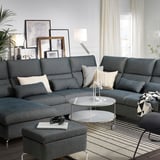 Modern living room with gray FAMMARP sectional sofa, glass coffee table, cushions, headphones, books, lamp, plants, and framed art. ”
