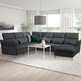 Dark grey l-shaped sectional sofa with adjustable headrests and wooden legs, against a white rug and wall, with a white coffee table.