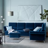 Modern living room with blue FAMMARP sofa, grey rug, white pendant light, and geometric artwork.