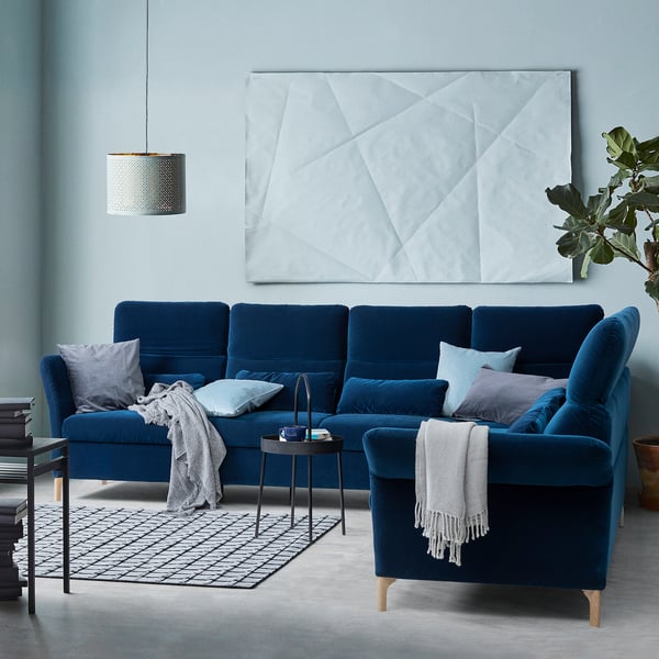 Modern blue velvet sectional sofa with gray pillows and throws, geometric rug, hanging lamp, and large wall art.