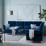 Modern blue velvet sectional sofa with gray pillows and throws, geometric rug, hanging lamp, and large wall art.