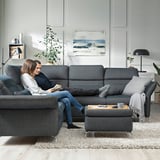 Two relax on sectional couch with adjustable headrests and footstool. Modern living room with rug, coffee table, and wall art.