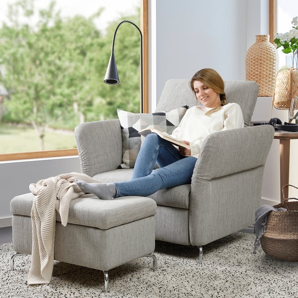 Woman reads on FAMMARP sofa by window, with footstool and lamp.