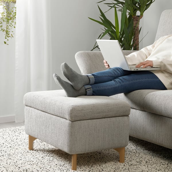 Person sits on FAMMARP footstool, working on laptop with feet up, showcasing its comfort and flexible use.